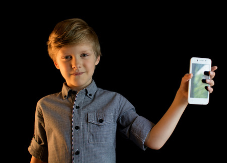 Smiling boy showing mobile phone. Isolated. Looking at camera. Black background.の写真素材