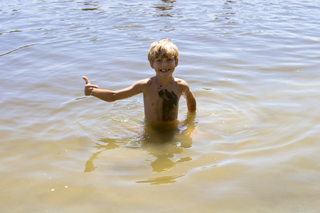A boy standing in the water shows his thumb up, as well as an index finger points. He is merry.の写真素材