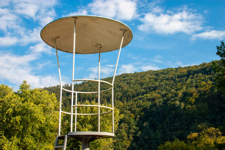 empty old metal lifeguard seat at a public swimming pool in germany in front of a green forrest...