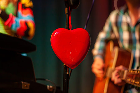 A heart as decoration on a microphone stand on a concert stage with blurred musicians in the...
