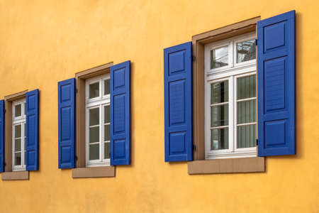 three white windows with sandstone sills in a row with dark blue shutters and a house wall painted orange yellowの写真素材
