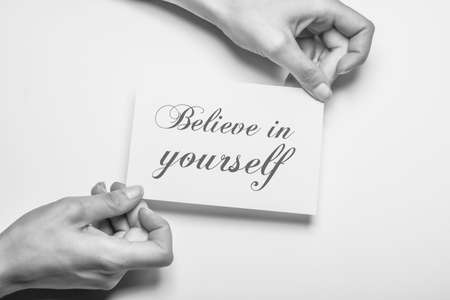 black and white photo of female hand holding a piece of paper with the inscription believe in yourself as a motivationの写真素材