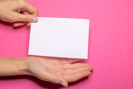 female hand holds a blank piece of paper with copy space in front of a Hot Pink background cardboard with the hand making a presenting gestureの写真素材