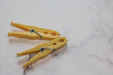 Two yellow classic plastic clothespins with copy space to the right from a surface with marble structureの写真素材