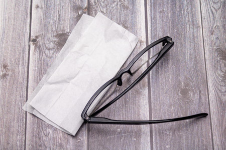 Top view of reading glasses with black temples and glasses cleaning cloth on rustic wood surfaceの写真素材