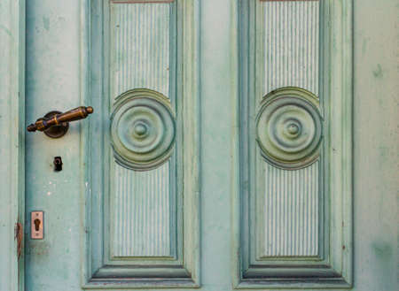 old mint green lacquered wooden door with coffered decorations and strong traces of useの写真素材