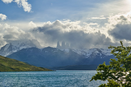 Towers of torres del Paine national park covered in clouds with dark green forest a lake and snow covered mountains of the Andes in Patagonia southern Chileの写真素材