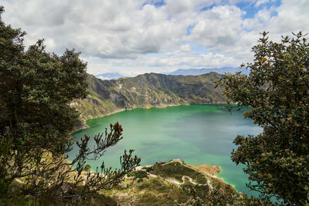 Beautiful quilotoa crater lake in Ecuador, South America with turquoise water inside a volcanic caldera with snow capped andes mountains in the background is famous for hikers and back packersの写真素材