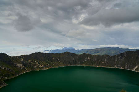 Beautiful quilotoa crater lake in Ecuador, South America with turquoise water inside a volcanic caldera with snow capped andes mountains in the background is famous for hikers and back packersの写真素材
