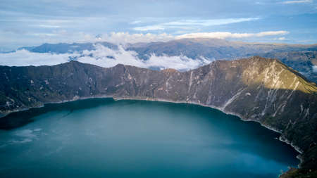 Aerial of beautiful quilotoa crater lake in Ecuador, South America with turquoise water inside a volcanic caldera with snow capped andes mountains in the background, famous for hikers and back packersの写真素材