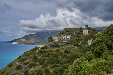 Coastline of the island of Corsica with high cliffs, old buildings and dense forest