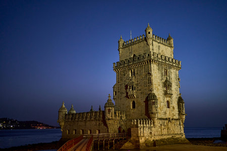 View at the illuminated Belem tower at night along the bank of Tagus River in Lisbon, Portugal,...
