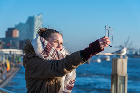 A young woman taking selfie with smart phone on Hamburg harborの写真素材