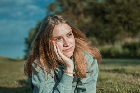 A young woman lies on the grass and braces her head and looks thoughtfulの写真素材