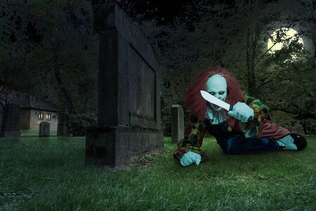a scary clown with a knife on a cemetryの写真素材