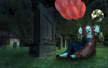 scary clown with ballons in his hand on a cemetryの写真素材