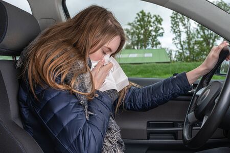 A young woman sneezes while driving car in a handkerchiefの写真素材