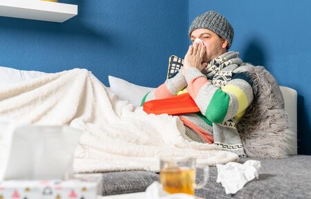 a man suffering from flu lies on the couch in the living roomの写真素材