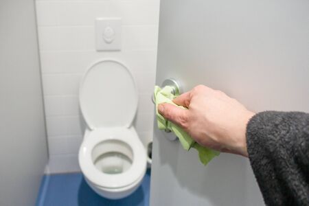 a hand cleans the door handle on a public toilet with a clothの写真素材