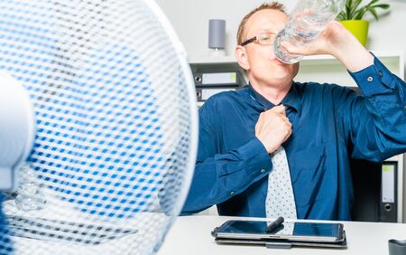 a thirsty businessman works in the office on a hot day and sweatsの写真素材