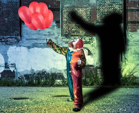 a clown with red balloons in front of a wall with shadowの写真素材