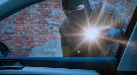 car thief examines a car with a flashlight at nightの写真素材