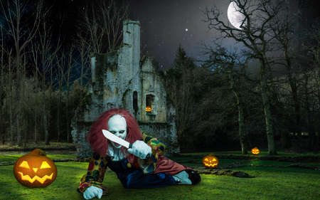 a scary halloween clown in front of an old building threatens with a knifeの写真素材