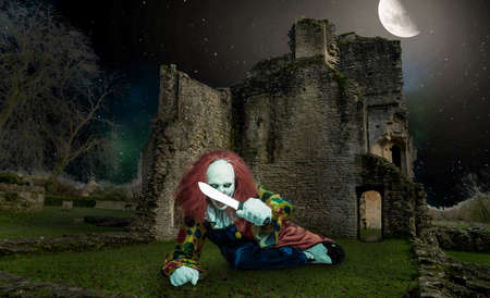 an evil halloween clown with a knife in front of an old castle at nightの写真素材
