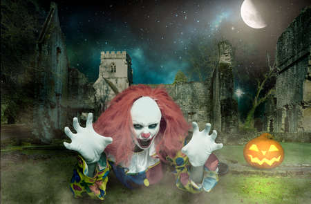 a terrifying clown in the ghostly surroundings stretches his hands threateningly forwardの写真素材