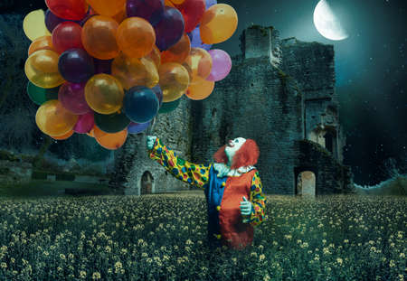 a clown is holding lots of balloons against a creepy backgroundの写真素材