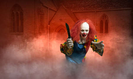 A clown with a knife in hand in front of a scary sceneの写真素材