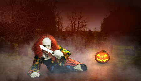 a clown threatening with a knife on a cemeteryの写真素材