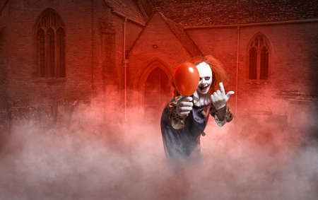 a scary clown with a balloon in front of a church is luring the viewerの写真素材