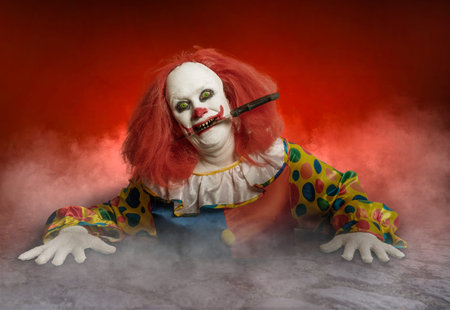 a scary clown with a knife in the mouth rising from the sewer
