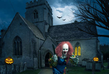 an evil clown with a knife in front of an old churchの写真素材