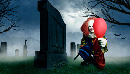 an evil clown with a knife and a balloon in a cemeteryの写真素材