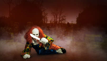 a crazy clown with a knife against the abstract background of a cemeteryの写真素材