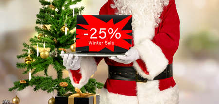 santa claus holds laptop in hand with 25 percent winter sale advertisingの写真素材