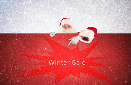 Santa claus points with his finger at a red board with the text winter saleの写真素材