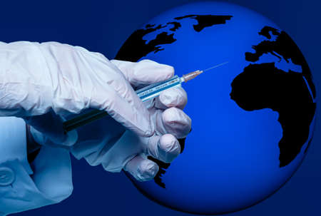 a hand holds a syringe with the inscription covid 19 vaccine in front of globeの写真素材