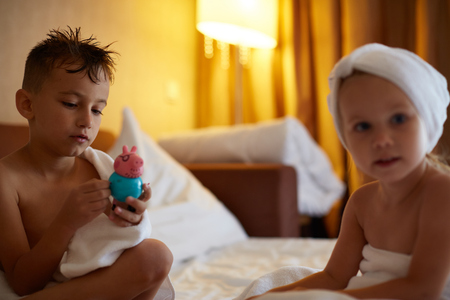 Child after bath. Cute little girl with wet curly hair wearing a bathrobe and head towel sitting on a white bed using lotion and brush. Hygiene for kids. Bathroom textile for babies and children.の写真素材