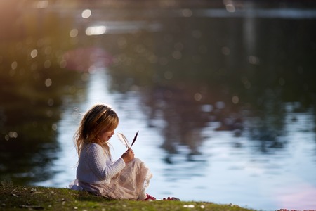 Girl sitting in the grass on the bank of the riverの写真素材