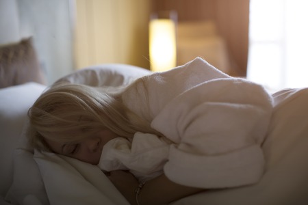 young girl in a white robe lying on the bedの写真素材