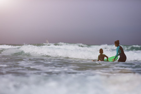 Athletic girl with little boy teaching him surfing