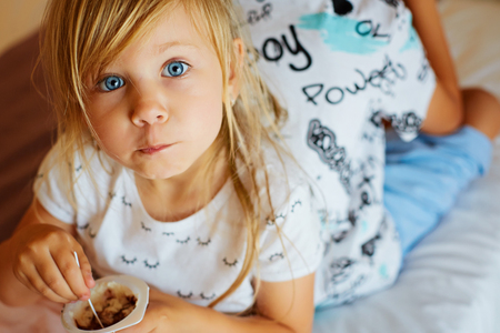 Little girl eating baby food isolated on blue backgroundの写真素材