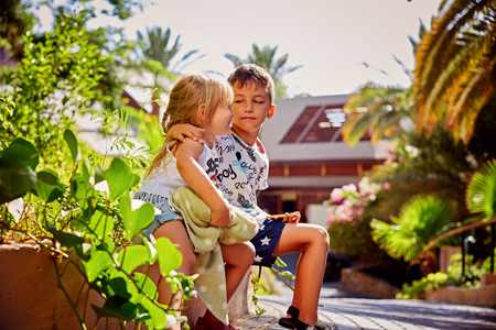 Two young caucasian children hugging and girl is kissing a boy on a cheek. They are sitting in a wooden house at playground, at sunny summer day.の写真素材