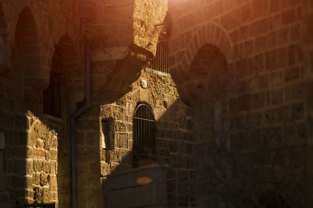 Stunning view of the street in old town of Ulcinj on sunset. Pots with flowers standing on paved pavement along stone wall. The sun light on stone arch. tel aviv, jaffaの写真素材