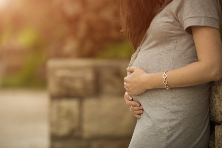 pregnant woman in grey dress holds hands a stomachの写真素材