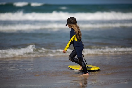 Happy girl - young surfer with bodyboard has fun on sea sand beach with waves. Family lifestyle, people water sport lessons, swimming activity on summer surf camp vacation with child in ocean island.の写真素材