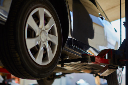Car lifted in automobile service for fixing, worker repairs detail, telephotoの写真素材